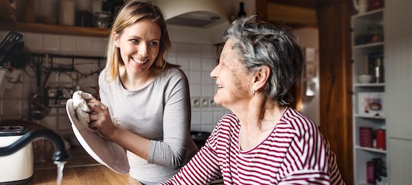 An elderly grandmother with an adult granddaughter at home, washing the dishes.