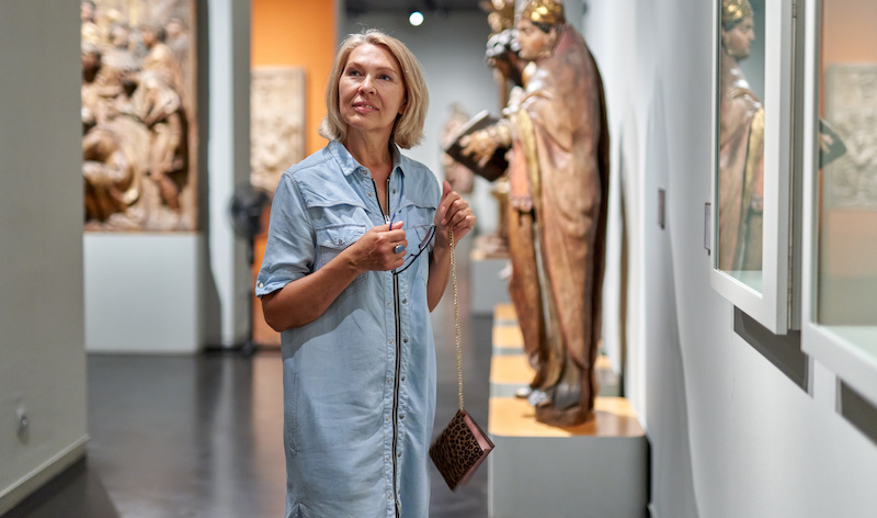 senior woman visitor looking at exhibition in museum of ancient sculpture