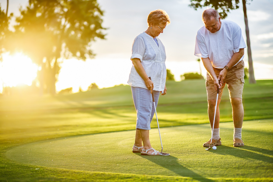 elderly couple playing golf together at sunset