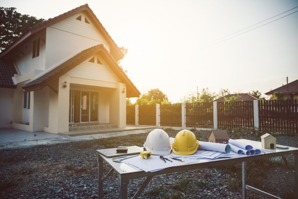 Photo of exterior of home with hard hats and blueprints